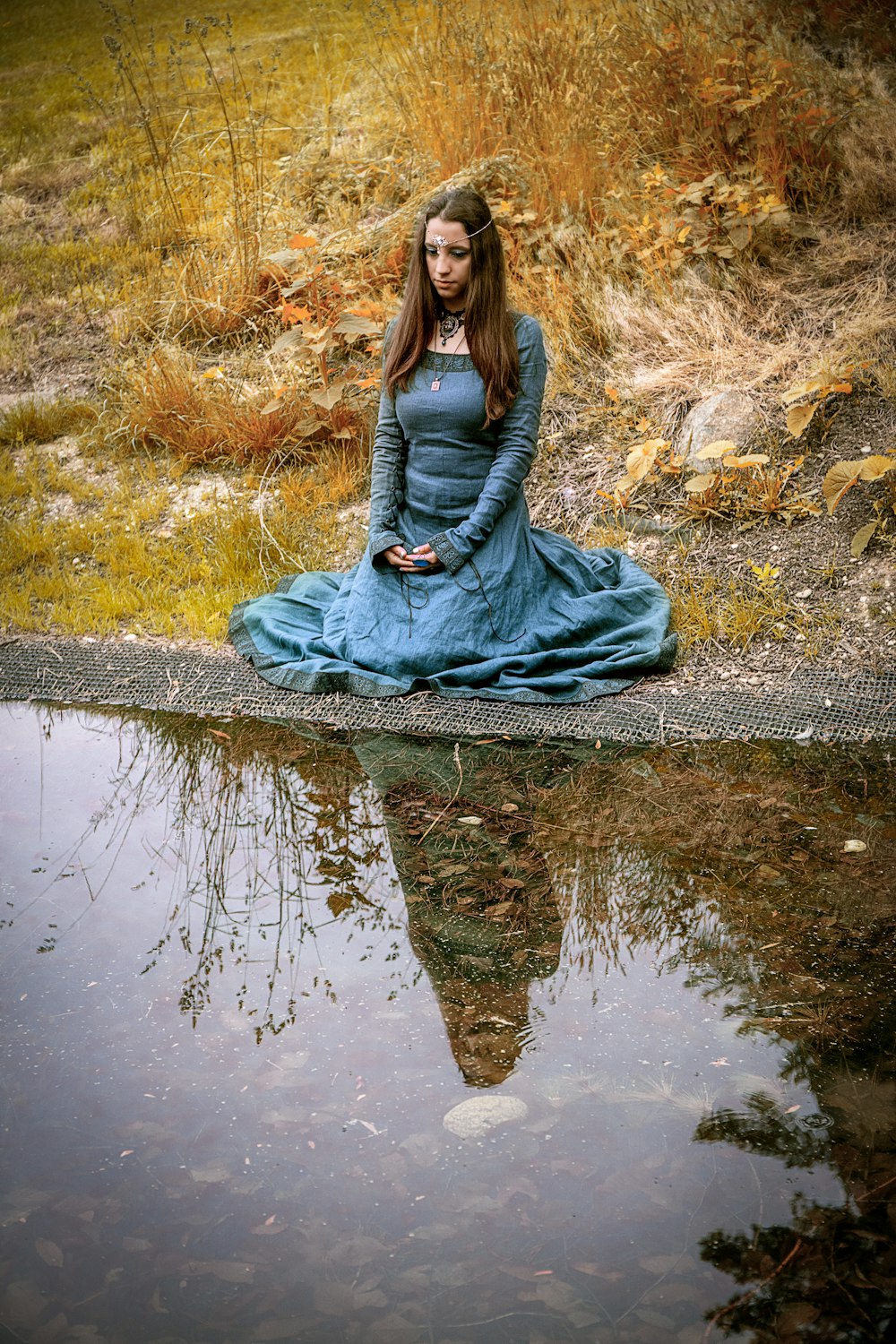 灰色の長袖ドレスを着た女性が昼間、川の近くの岩の上に座っている