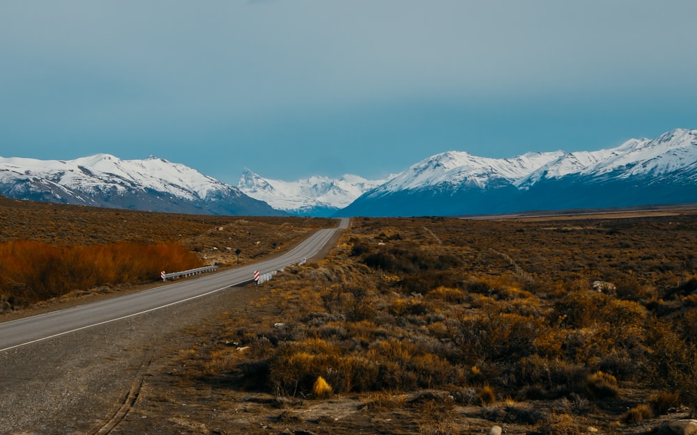 gray concrete road near snow covered mountains during daytime