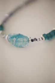 A close-up of a bracelet featuring a large turquoise stone as the centerpiece, interspersed with smaller silver beads and additional turquoise stones. The background is soft and out of focus, highlighting the texture and color of the bracelet.