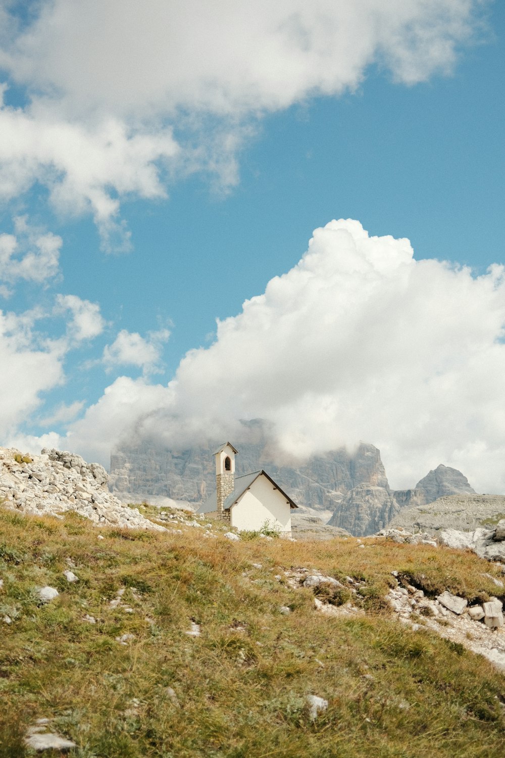 Casa bianca e grigia sul campo di erba verde vicino alla montagna rocciosa sotto nuvole bianche e blu