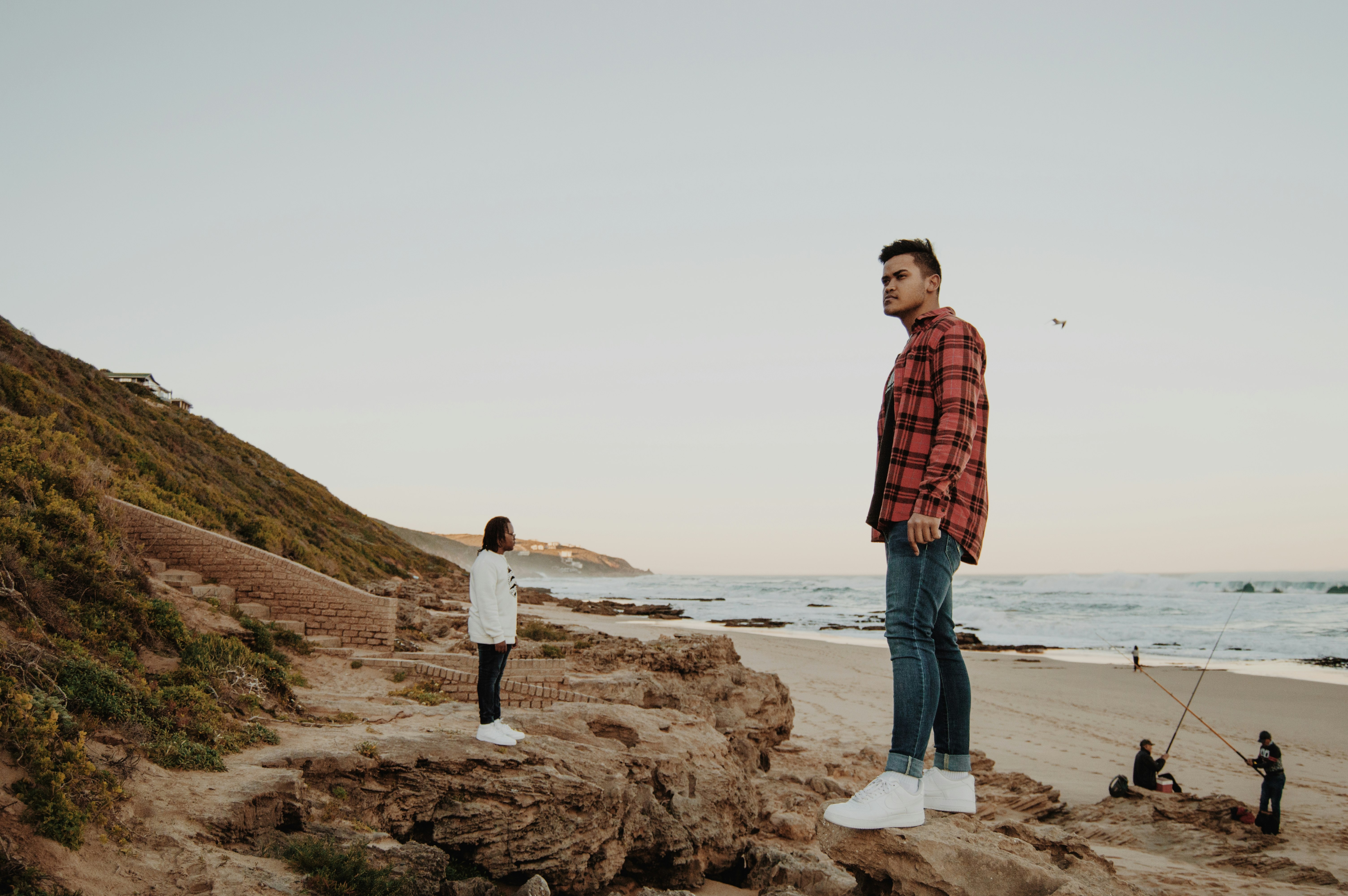 man in red and black plaid dress shirt standing on brown rock formation near body of during