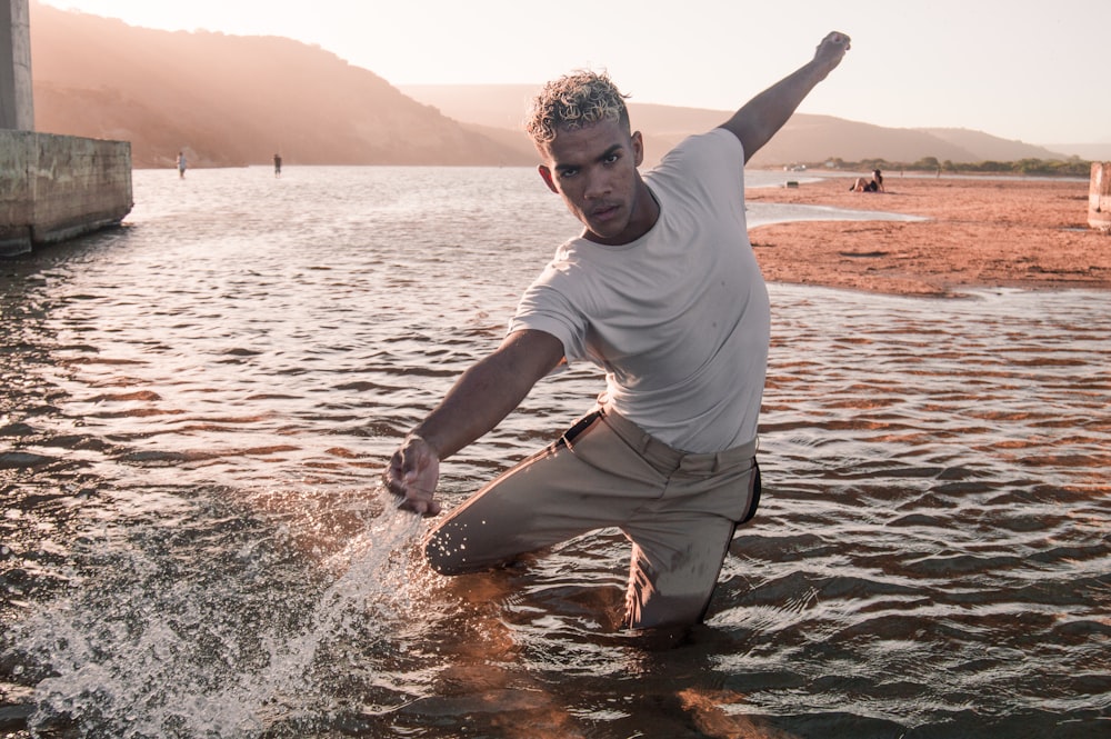 man in white crew neck t-shirt and brown shorts standing on water during daytime