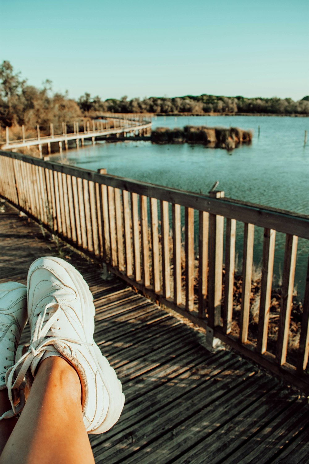 person in white sneakers sitting on wooden dock during daytime