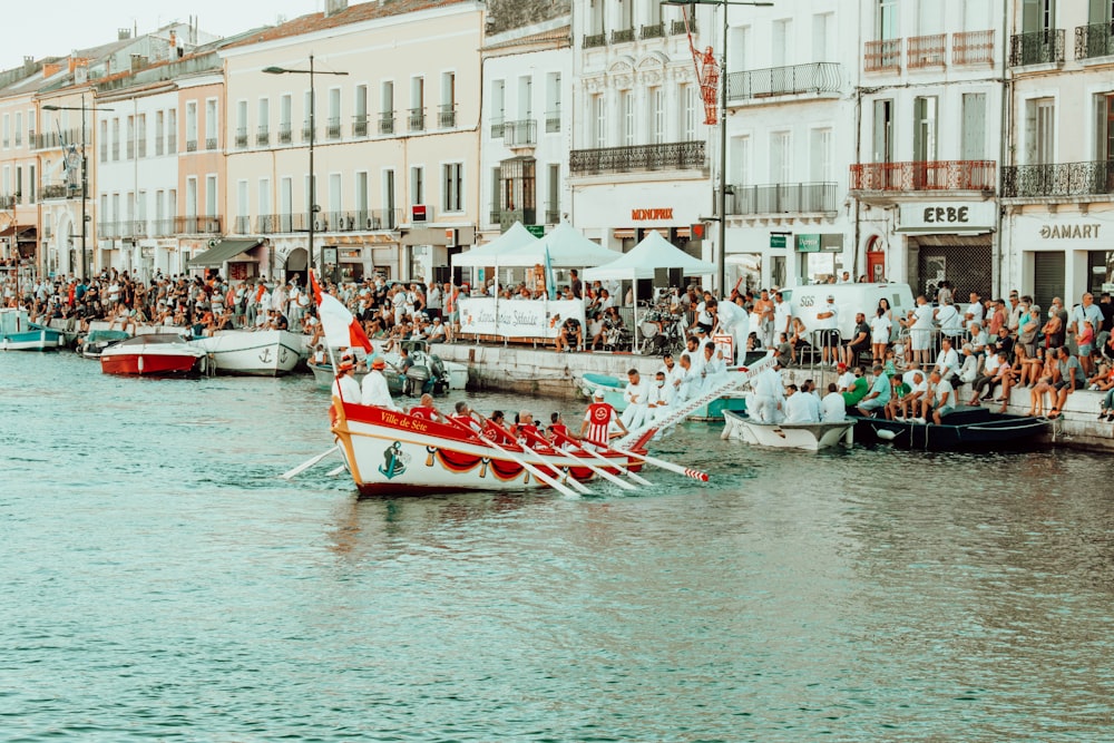 people riding on red boat on river near buildings during daytime