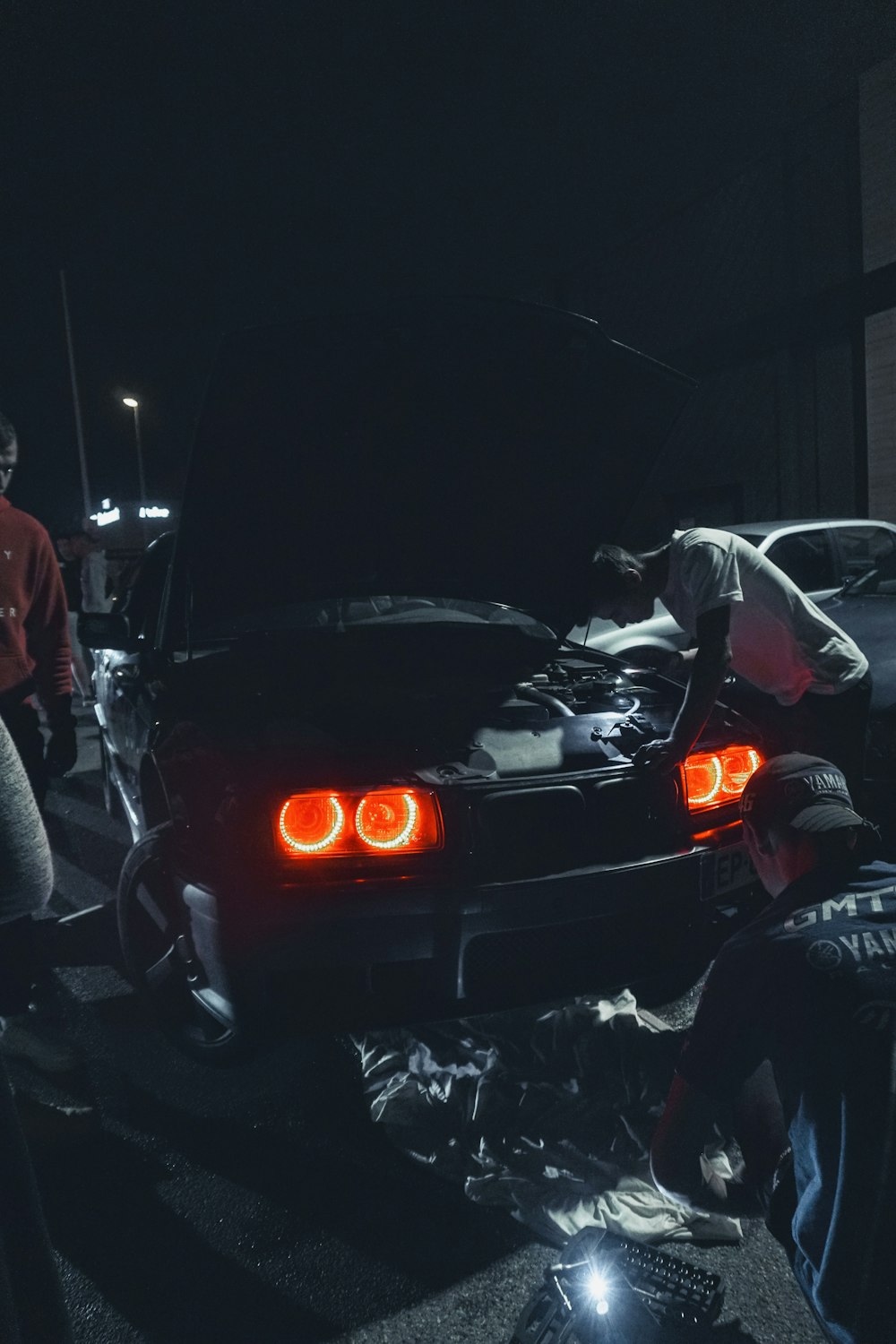 man in red jacket standing beside black car