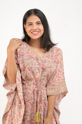 A person with shoulder-length dark hair and a joyful expression wearing a colorful, patterned garment made of lightweight fabric. The garment has a drawstring at the waist and features intricate designs in pink and green hues.