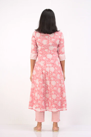 A confident plus-size Indian woman wearing a flowing blush pink kurti, smiling warmly against a soft beige background.