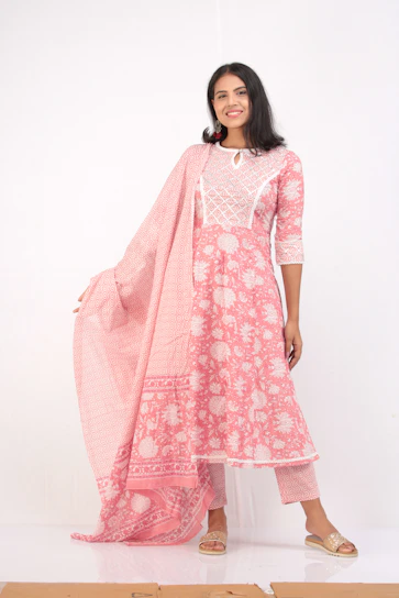 Elegant Pakistani woman in a flowing magenta suit, smiling confidently against a soft white background.