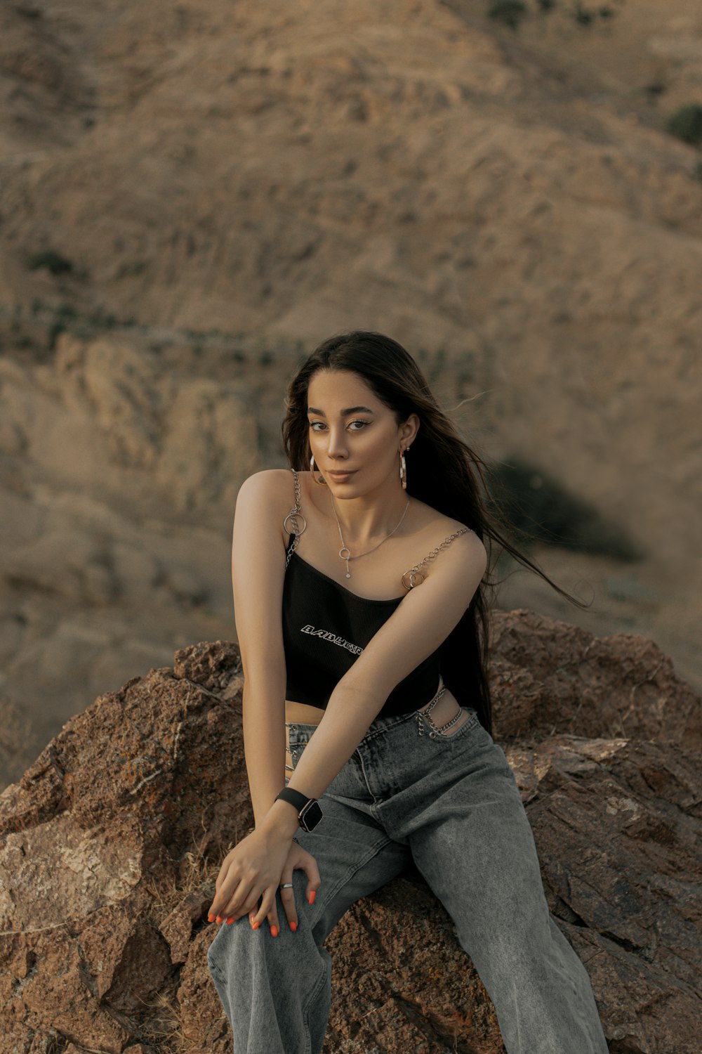 woman in black tank top and blue denim jeans sitting on brown rock