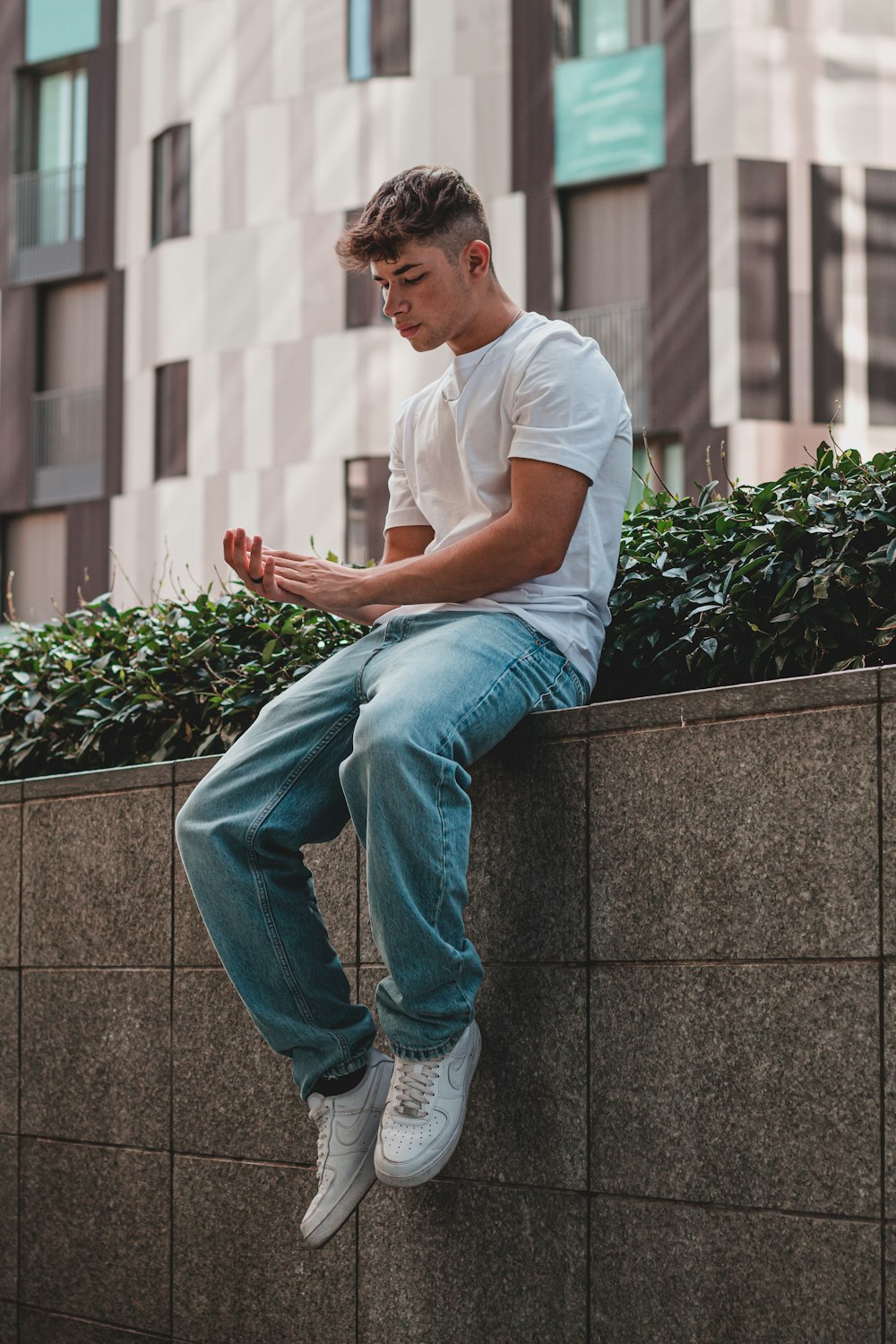 man in white crew neck t-shirt and blue denim jeans sitting on gray concrete bench