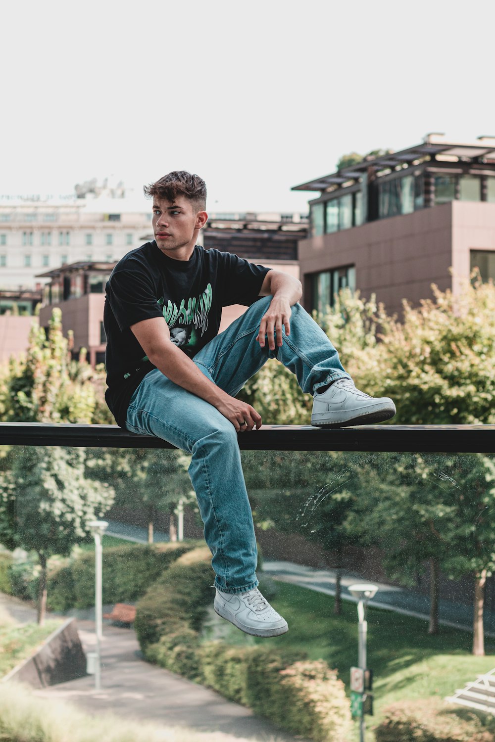 man in black crew neck t-shirt and blue denim jeans sitting on brown wooden railings