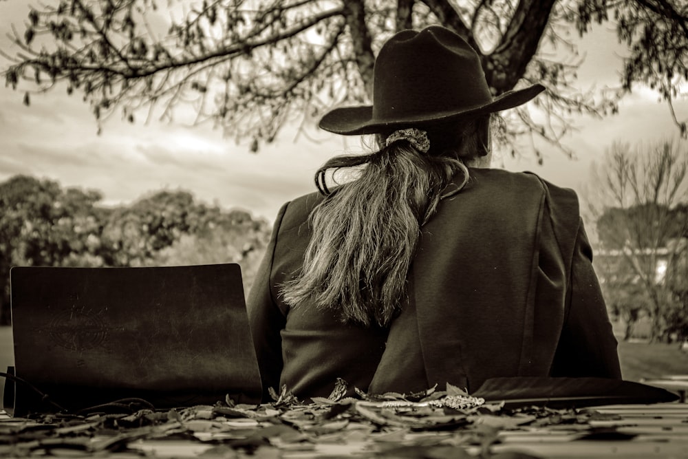 woman in black long sleeve shirt and black hat sitting on rock in grayscale photography