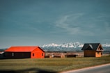 red and black barn near brown grass field and snow covered mountains during daytime