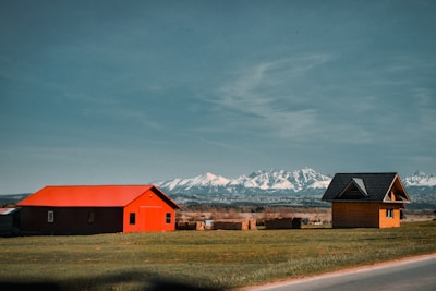 red and black barn near brown grass field and snow covered mountains during daytime