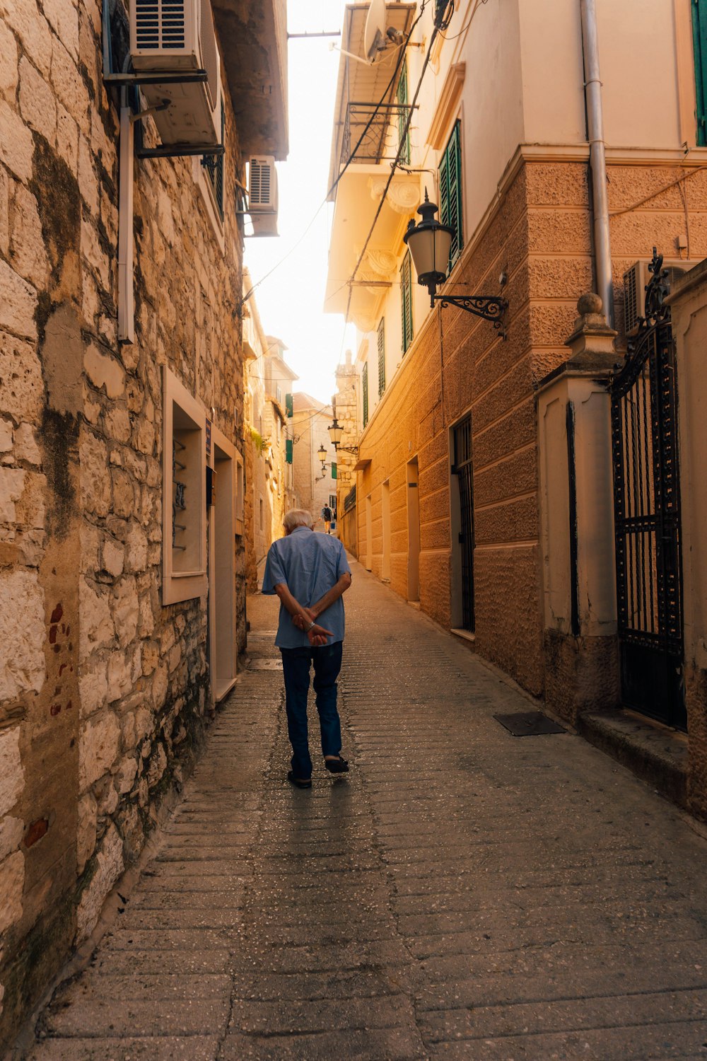 man in blue dress shirt walking on sidewalk during daytime