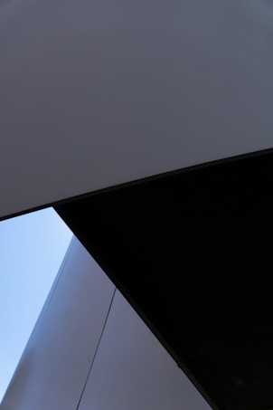 An abstract composition of geometric shapes with angular lines and contrasting dark and light surfaces. The image features a large dark triangular shape intersecting with lighter gray and blue sections, creating a sense of depth and modernity.