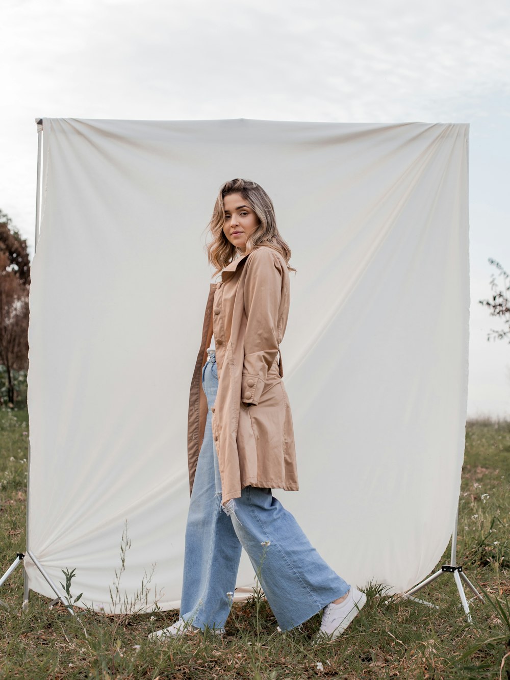 woman in brown coat and blue denim jeans standing on white textile