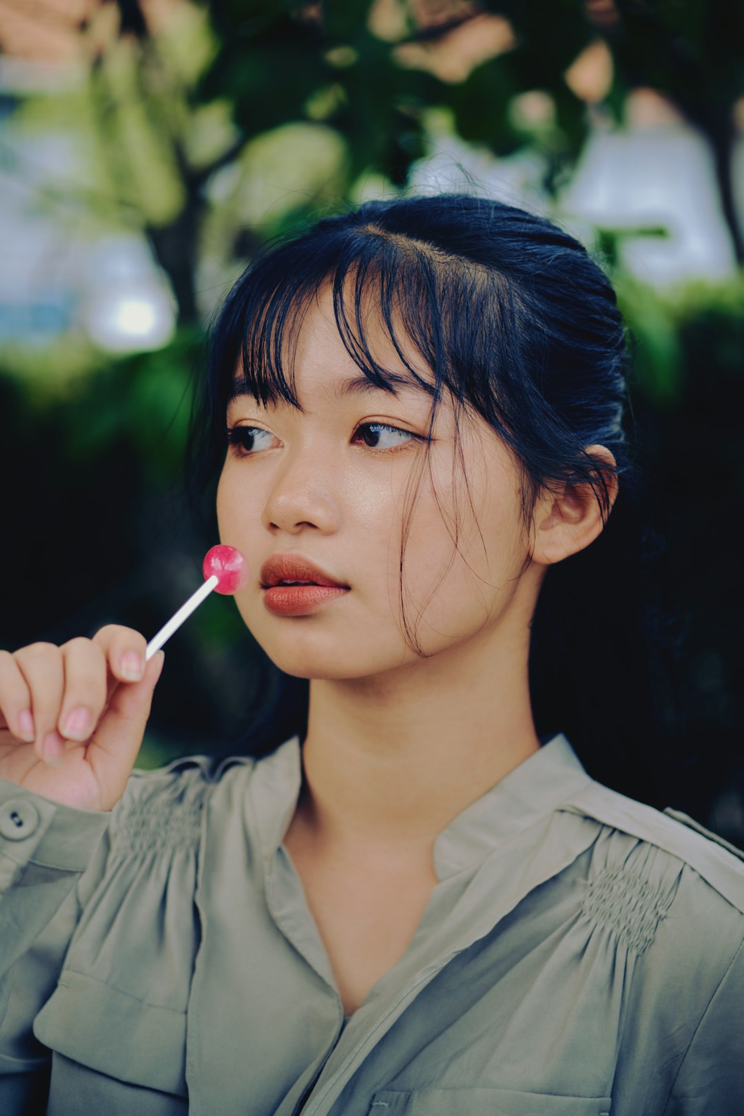 woman in gray button up shirt holding pink lollipop