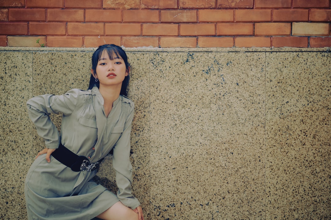 woman in gray coat leaning on brown brick wall