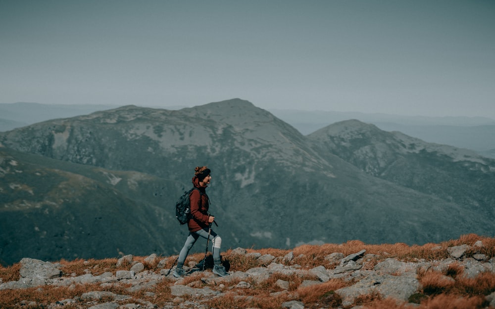 uomo in giacca nera e pantaloni neri in piedi sulla collina rocciosa durante il giorno