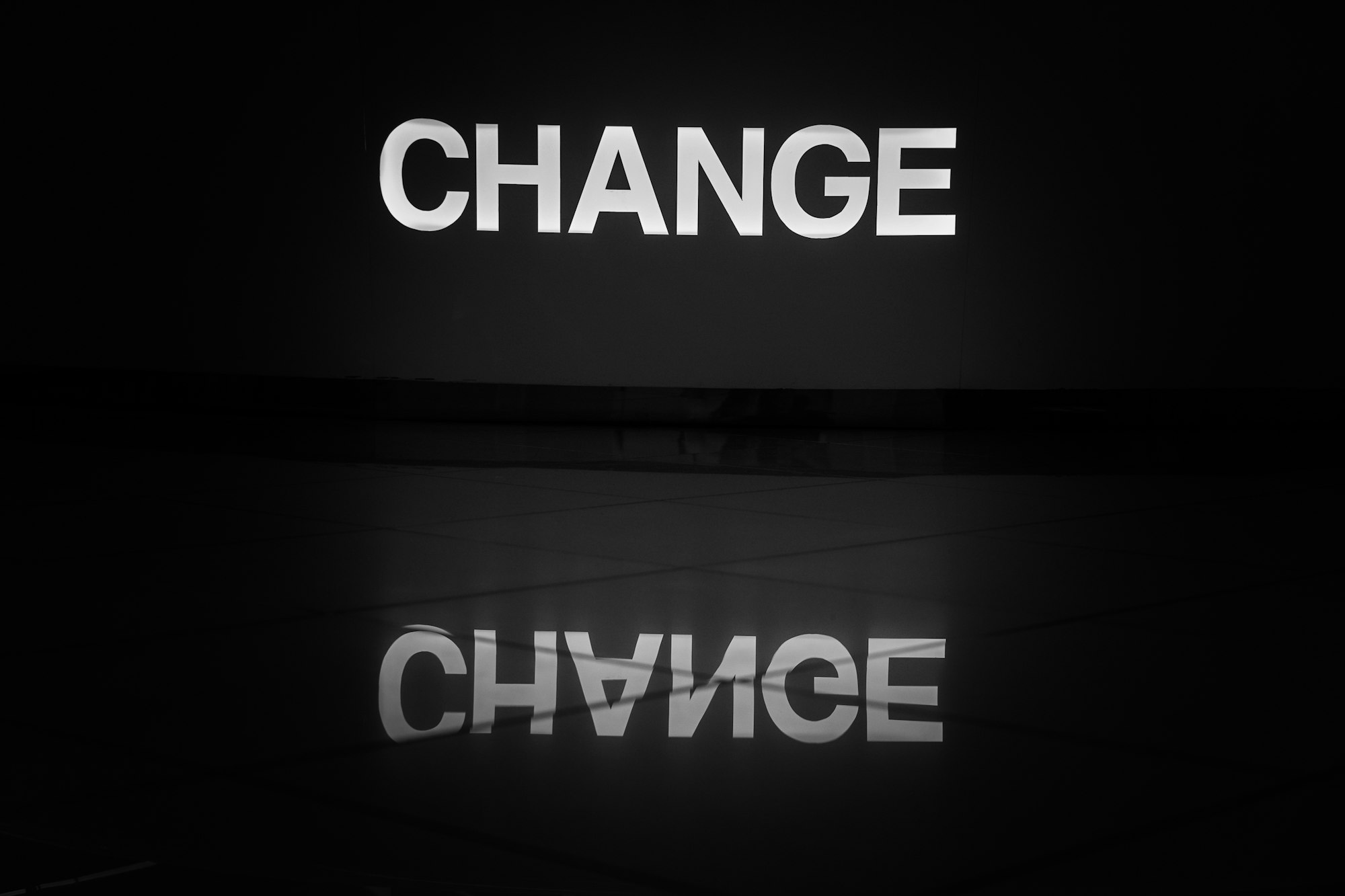 The word change illuminated in white and reflected on a tiled floor.