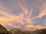 A wide shot of a mountain range under a dramatic cloudy sky at sunset.