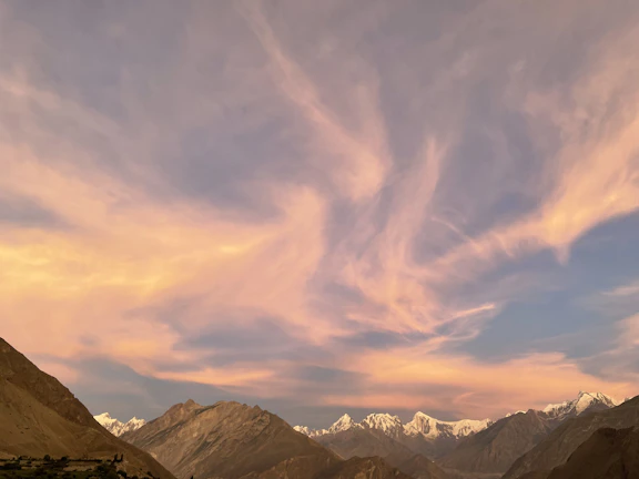 A wide shot of a mountain range under a dramatic cloudy sky at sunset.