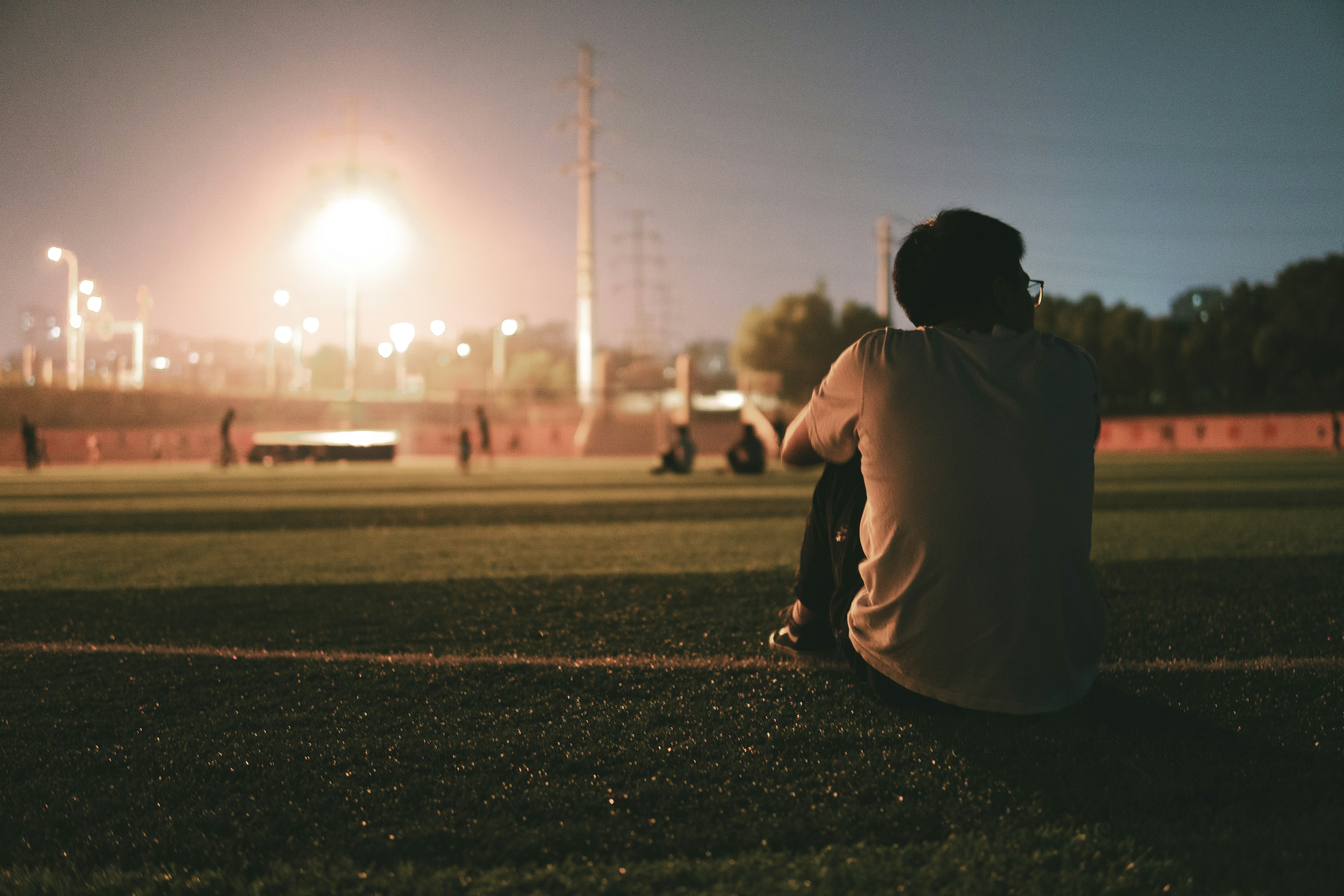 man in white hoodie sitting on green grass field during daytime