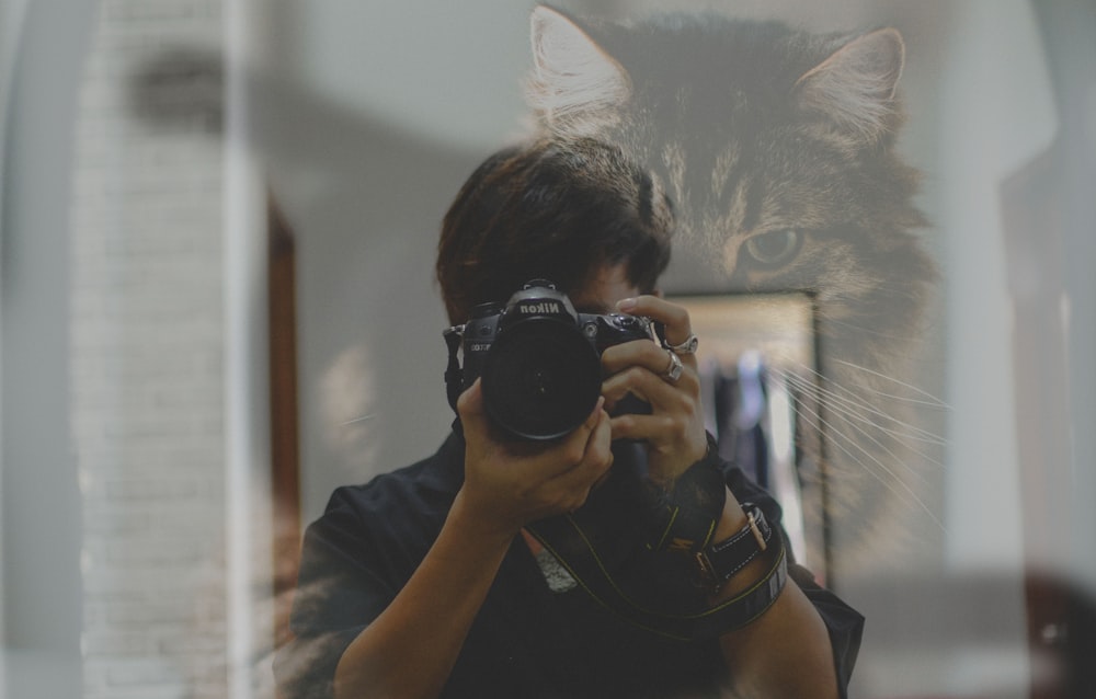 Hombre en camiseta sin mangas negra sosteniendo una cámara DSLR Nikon negra