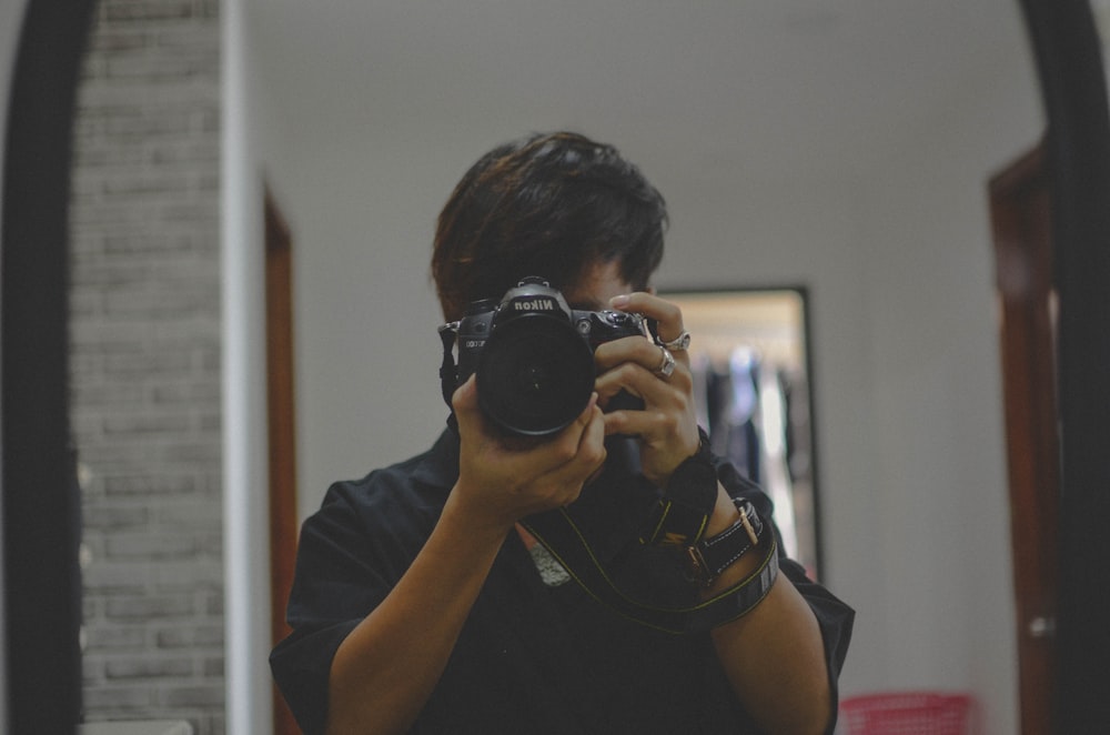 homem na camiseta preta do pescoço da tripulação segurando a câmera preta nikon dslr