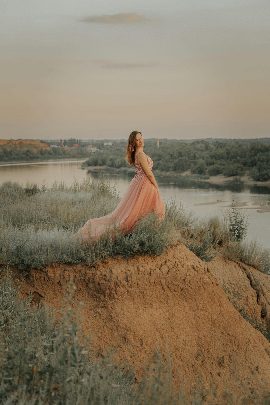 woman in pink dress standing on brown grass field near lake during daytime