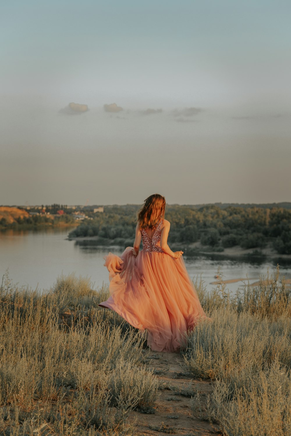 낮 동안 호수 근처의 푸른 잔디밭에 서 있는 갈색 드레스를 입은 여자