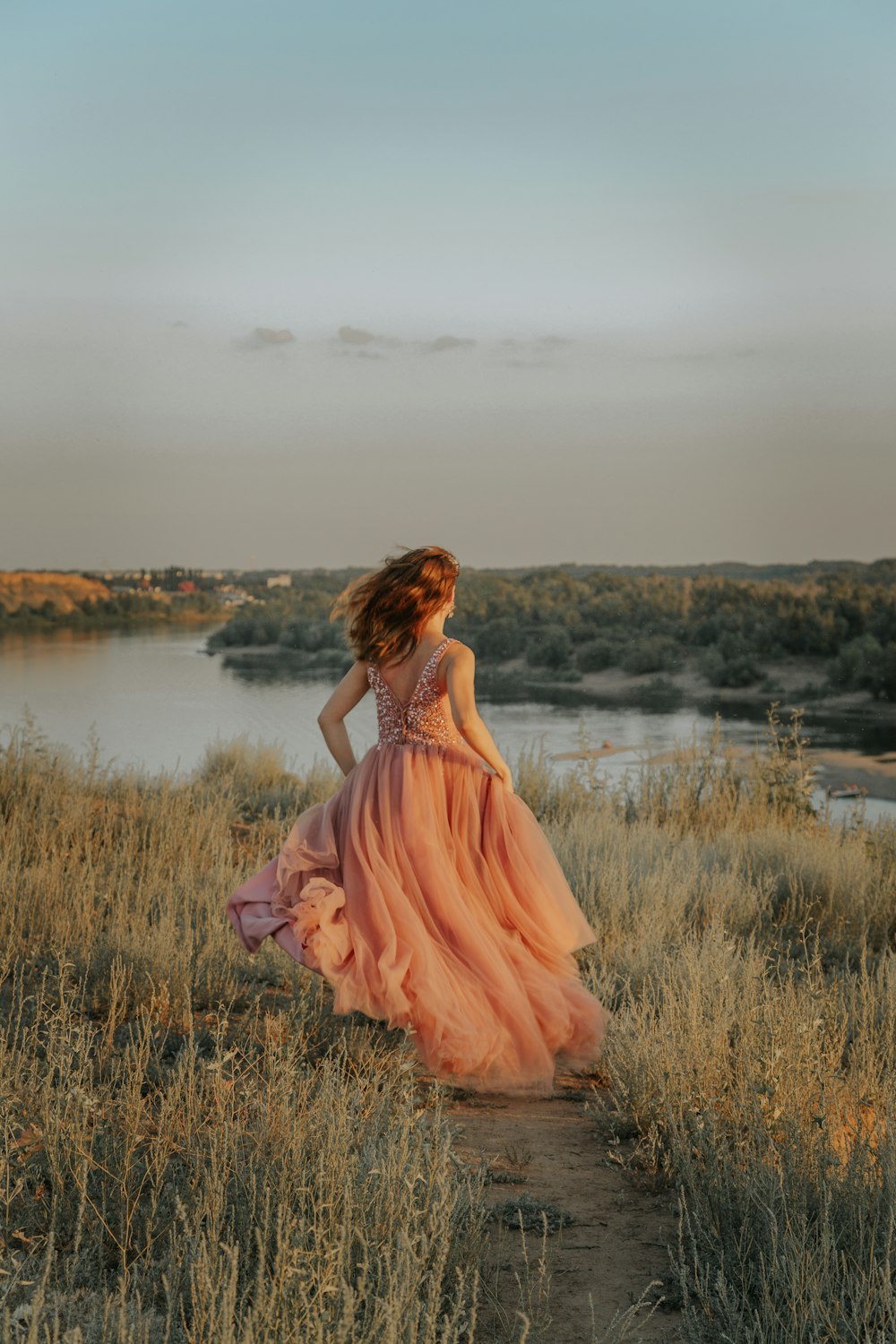 woman in pink dress standing on brown grass field near lake during daytime