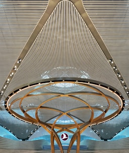 A modern architectural ceiling design featuring parallel lines and a central circular structure with golden arcs and embedded lights. A logo is suspended in the middle, creating a futuristic and symmetrical appearance.