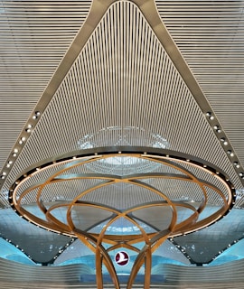 A modern architectural ceiling design featuring parallel lines and a central circular structure with golden arcs and embedded lights. A logo is suspended in the middle, creating a futuristic and symmetrical appearance.