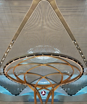 A modern architectural ceiling design featuring parallel lines and a central circular structure with golden arcs and embedded lights. A logo is suspended in the middle, creating a futuristic and symmetrical appearance.