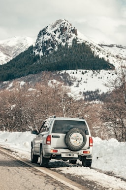black suv on snow covered ground near brown trees and snow covered mountain during daytime