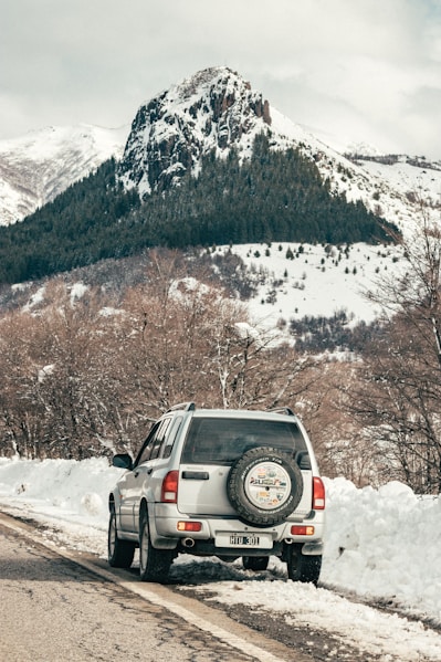 black suv on snow covered ground near brown trees and snow covered mountain during daytime