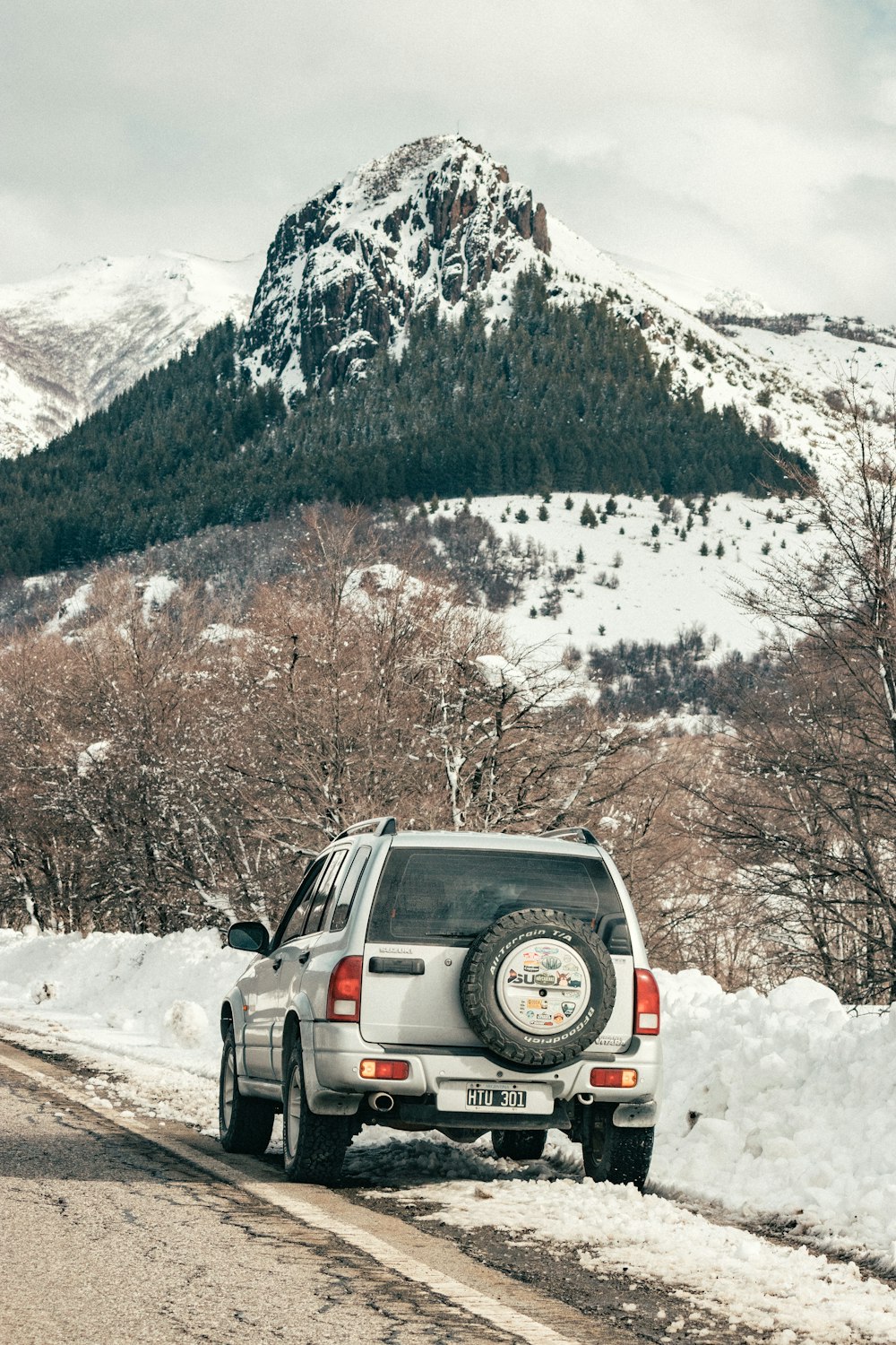 SUV negro en suelo cubierto de nieve cerca de árboles marrones y montañas cubiertas de nieve durante el día