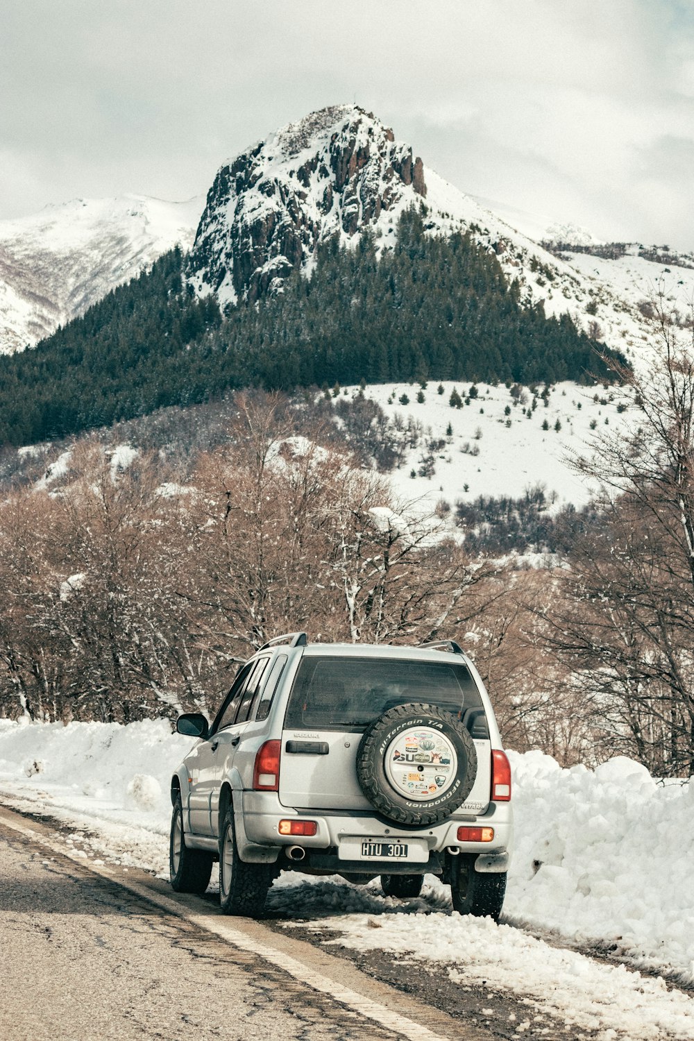 black suv on snow covered ground near brown trees and snow covered mountain during daytime