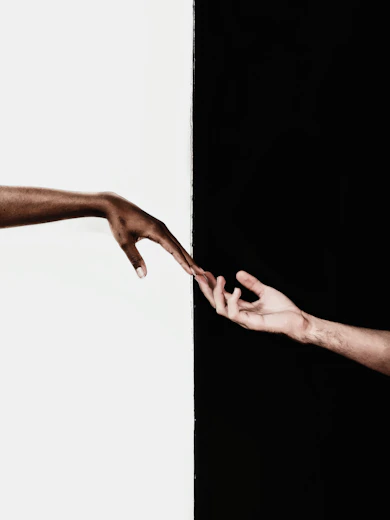 A black and a white hand touching in the center of the picture with a black and white backgound