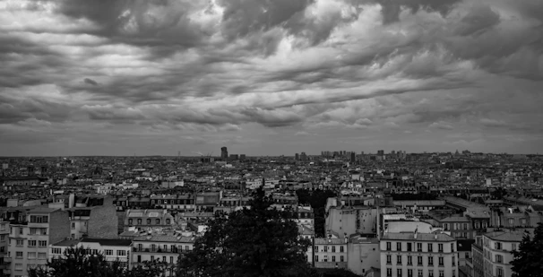 A dramatic black and white cityscape showing tall buildings under cloudy skies.