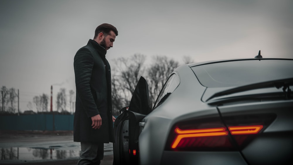 man in black jacket standing beside black car during daytime
