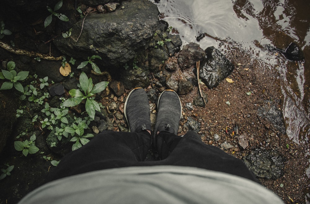 person in black pants and black shoes standing on rocky ground