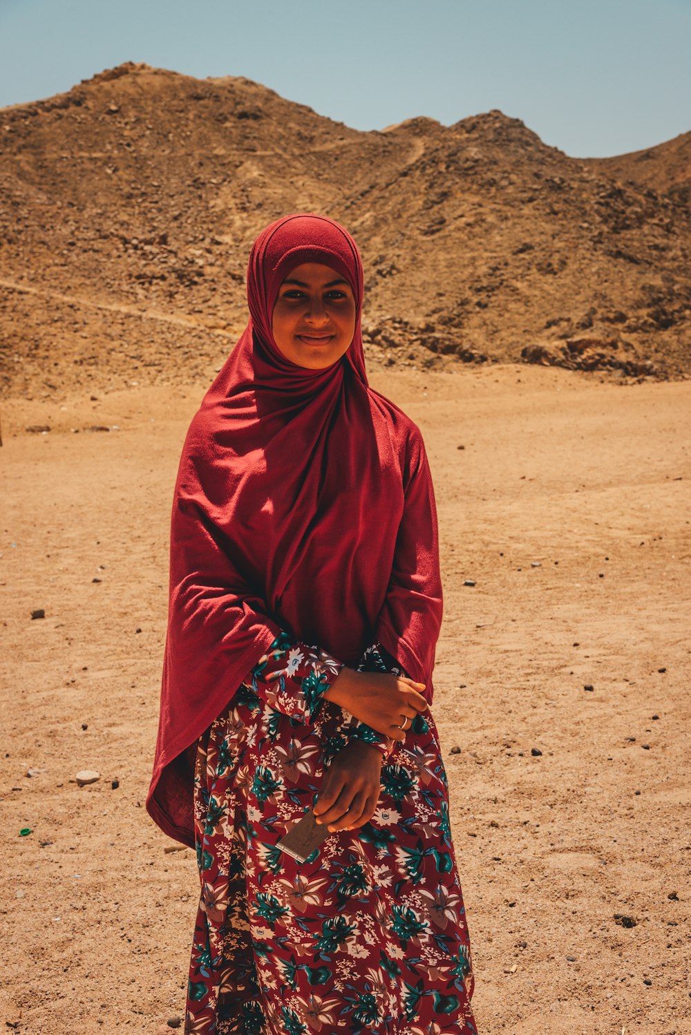woman in red hijab standing on brown sand during daytime