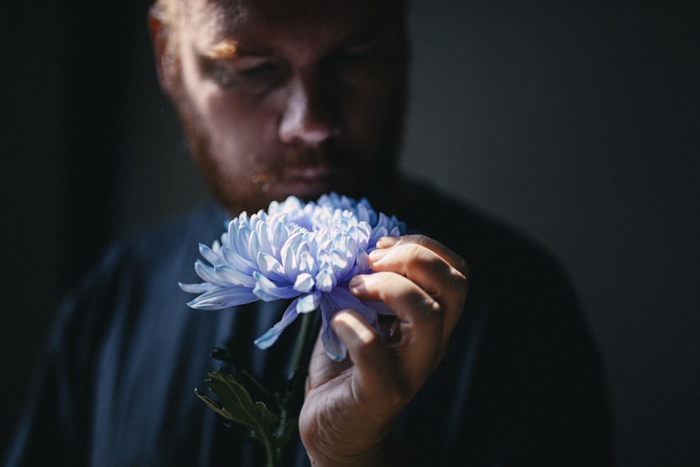 man holding blue flower in dark room