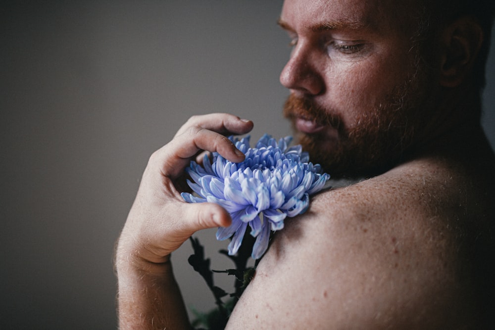 man in black and white floral shirt holding blue flower