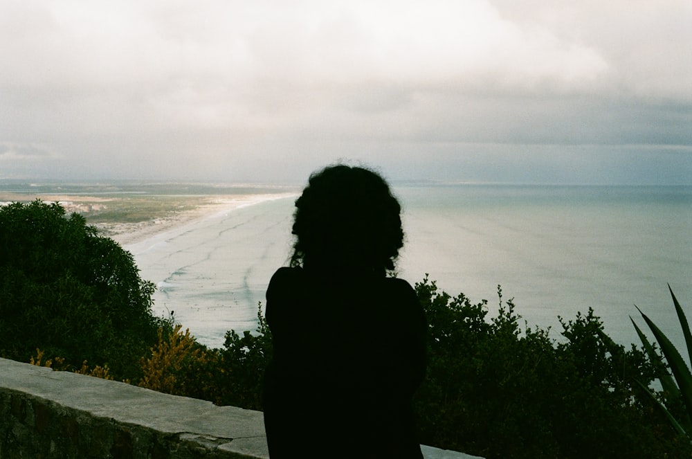 silhouette of woman standing on rock near body of water during daytime