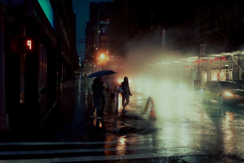 man and woman holding umbrella walking on sidewalk during night time