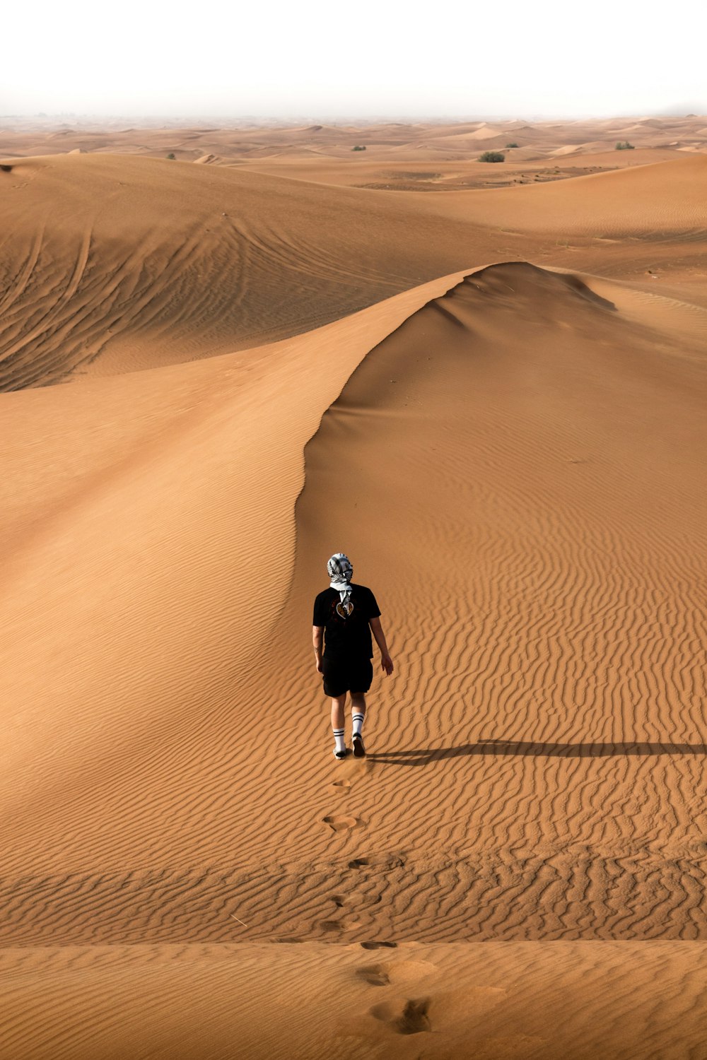 person in black jacket walking on brown sand